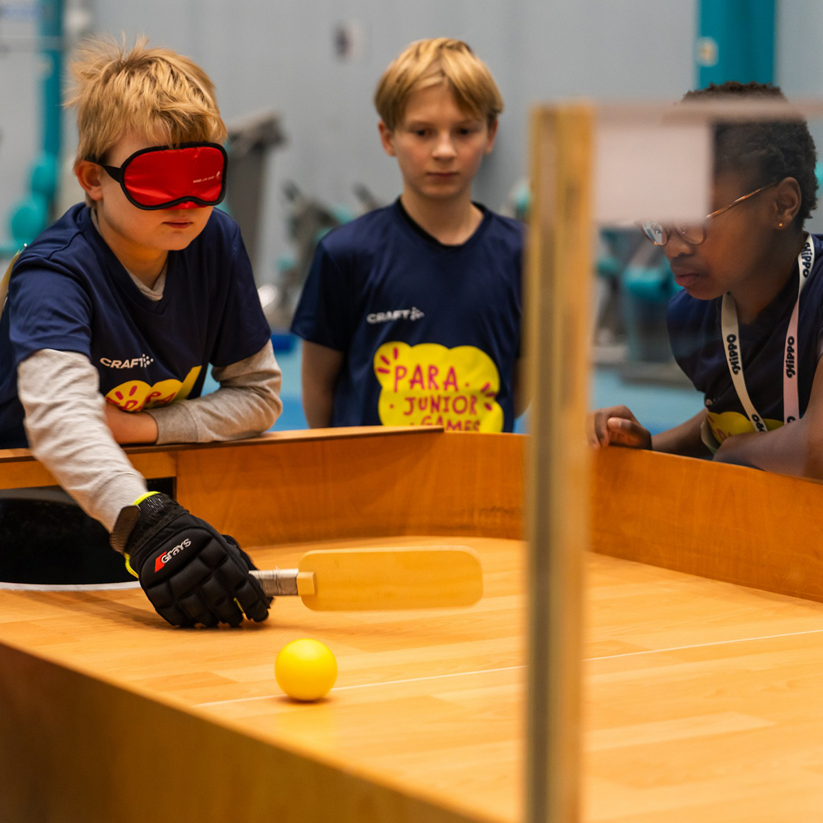 Poika pelaamassa sokkopingistä puisen pelipöydän päädyssä silmät peitettynä punaisella maskilla.